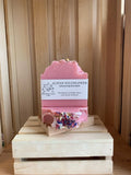 Alpine Wildflower handmade soap bars with pink color and dried flower pieces displayed on a wooden crate stand. 