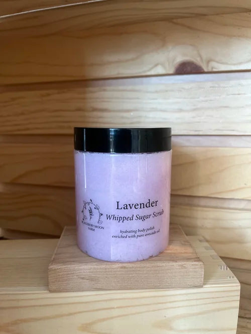 Lavender whipped sugar scrub body polish in a plastic jar with black lid displayed on a wooden stand. 
