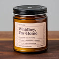 Whidbey, Im Home scented soy candle in amber glass jar with black lid on wood surface