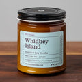 Whidbey Island scented soy candle in amber glass jar with black lid on wood surface