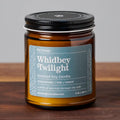 Whidbey Twilight scented soy candle in amber glass jar with black lid on wood surface